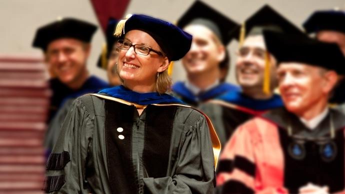 Jen Mathews in a cap and gown, smiling, surrounded by other professors